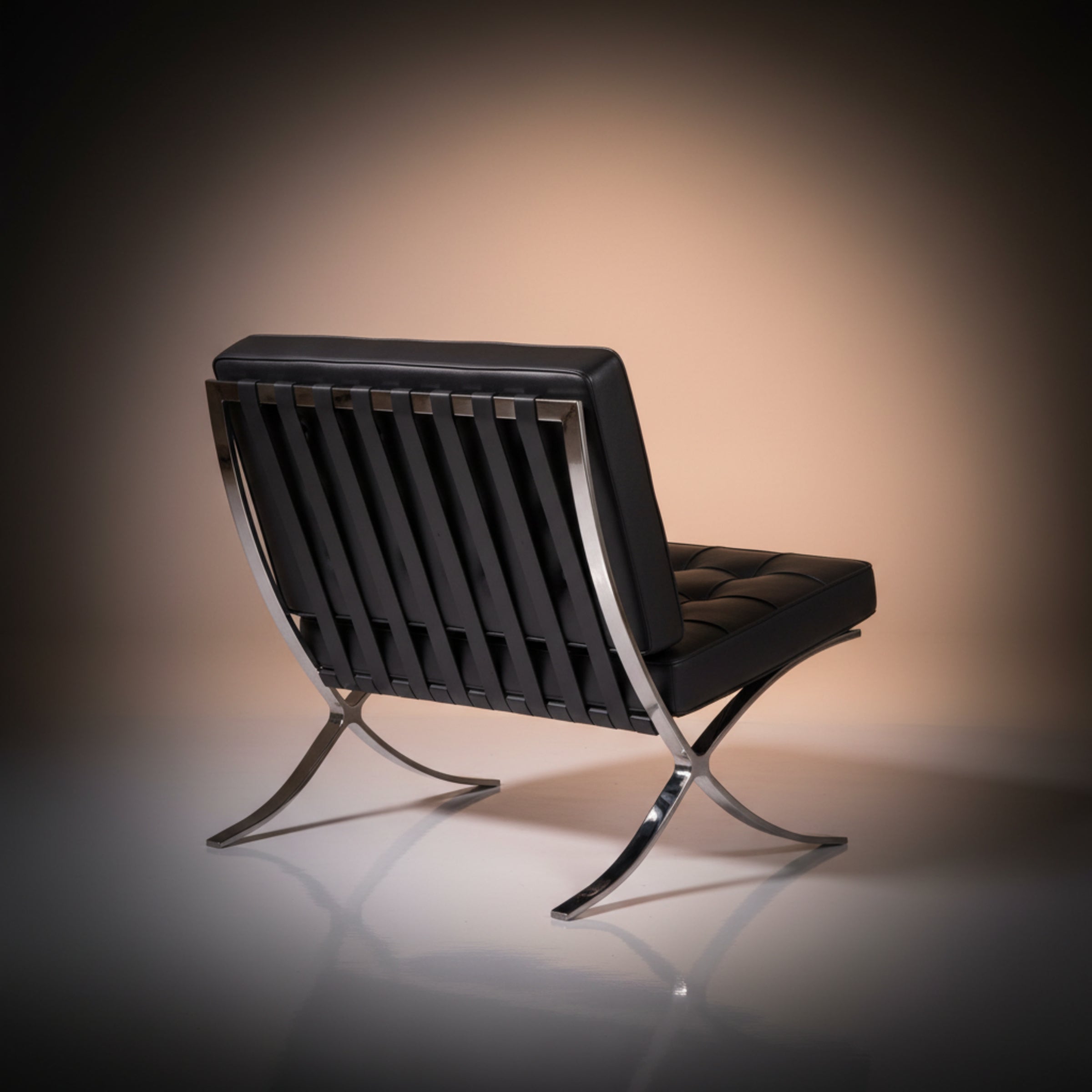A modern black leather lounge chair with a chrome metal frame and curved legs, photographed on a reflective surface.