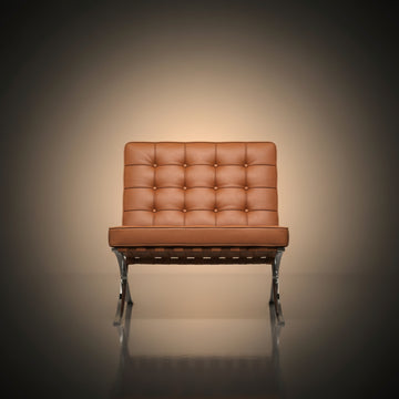 A modern leather armchair with a tufted backrest and chrome legs, centered against a dark vignette background with a warm spotlight effect.