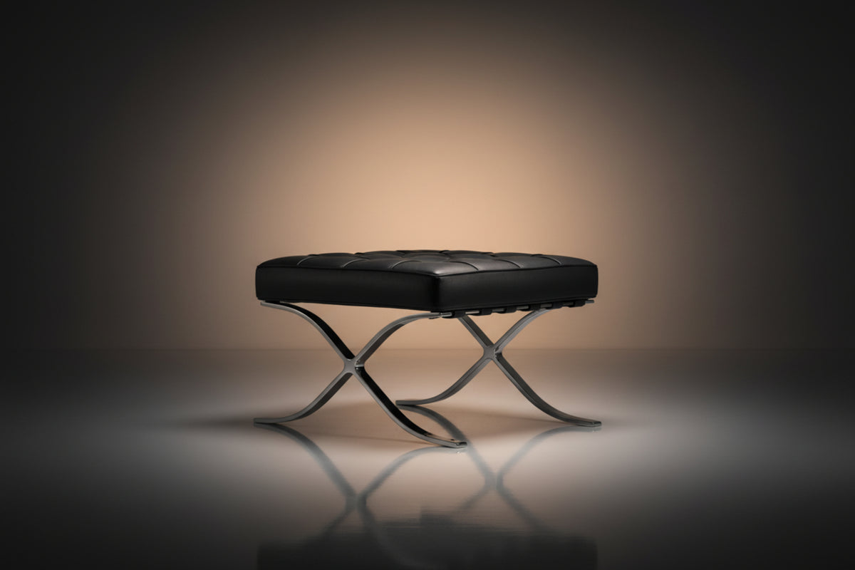 A modern black leather tufted ottoman or bench with an X-shaped polished metal base