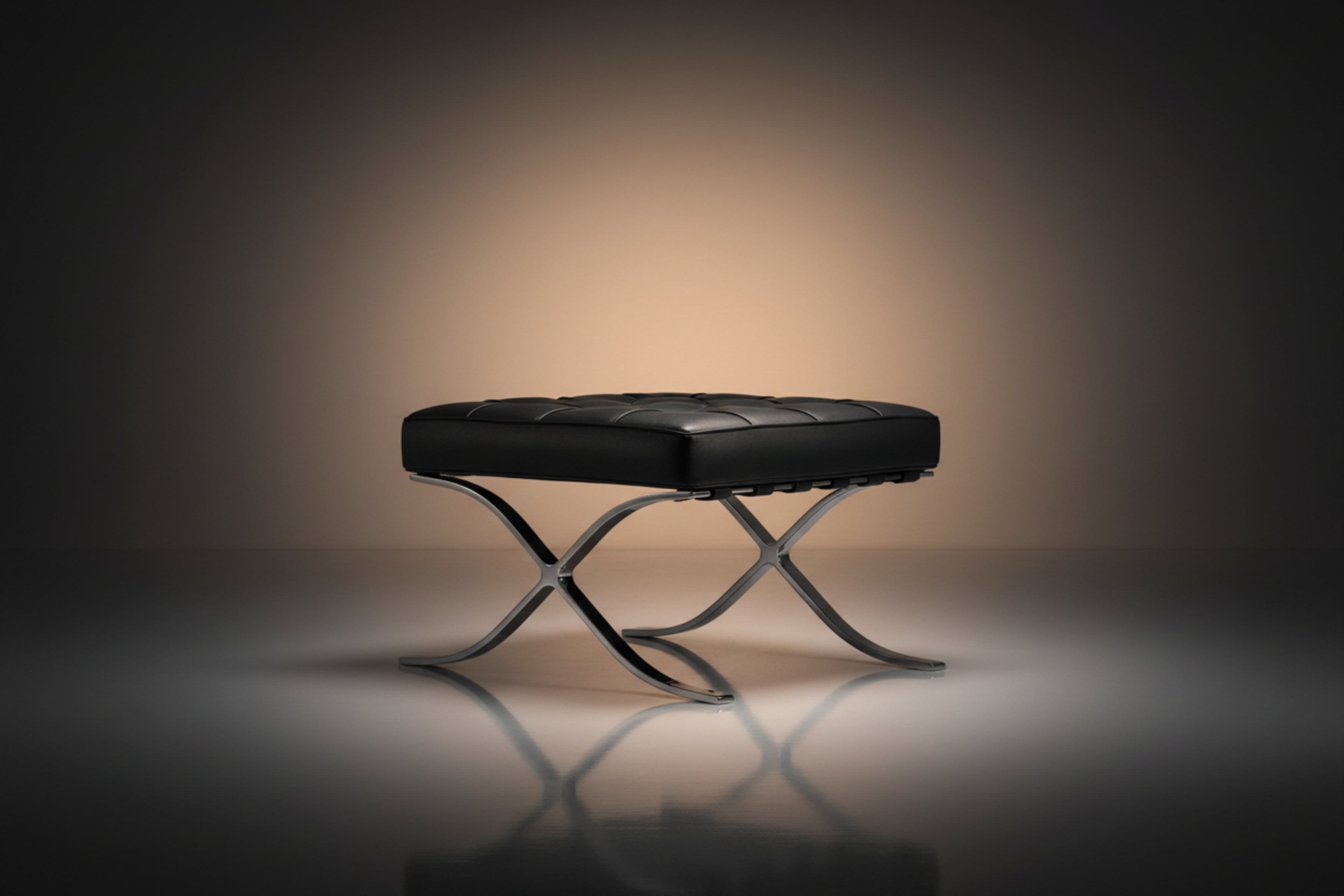 A modern black leather tufted ottoman or bench with an X-shaped polished metal base