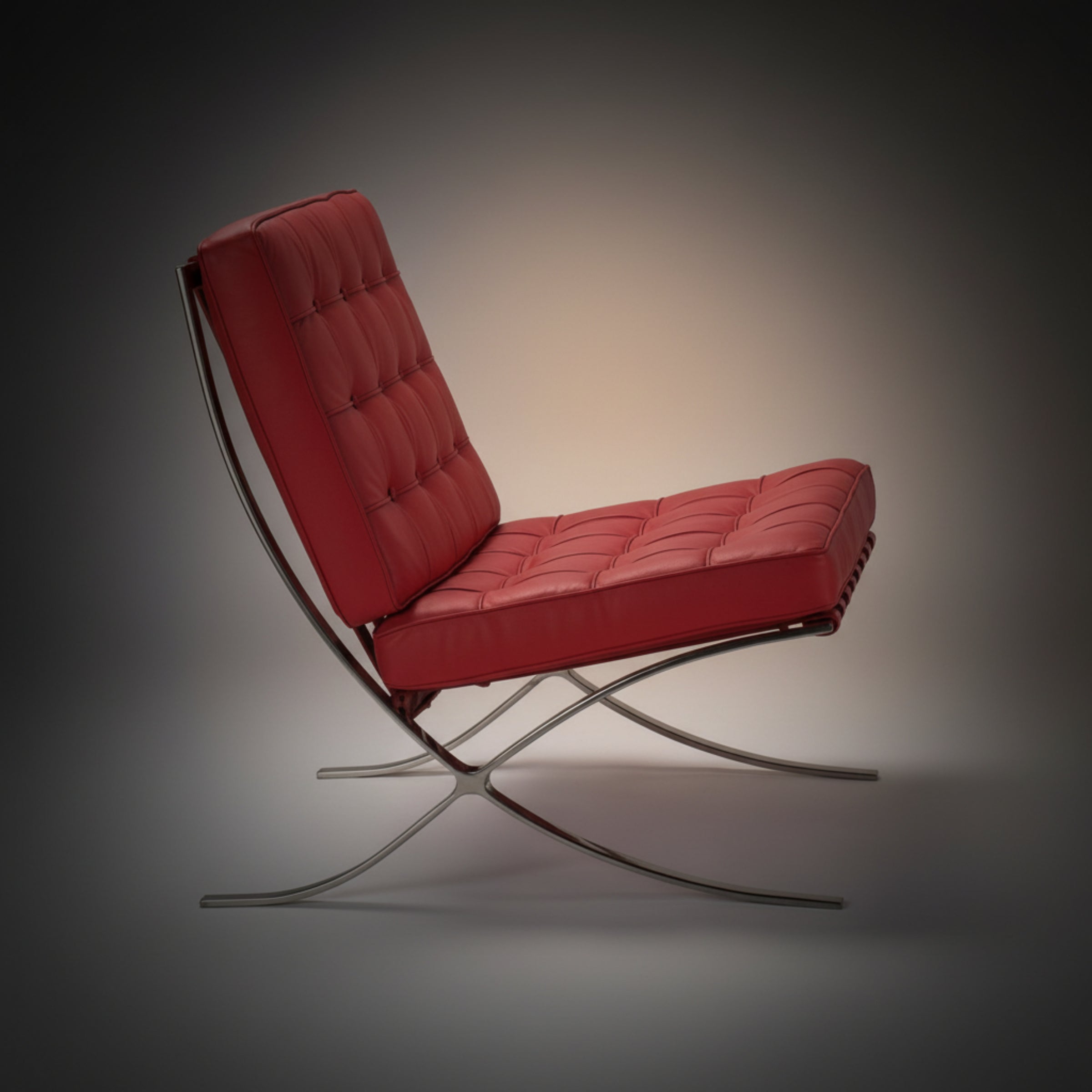 A modern red tufted leather armchair with a chrome curved metal frame, shown from a side profile.